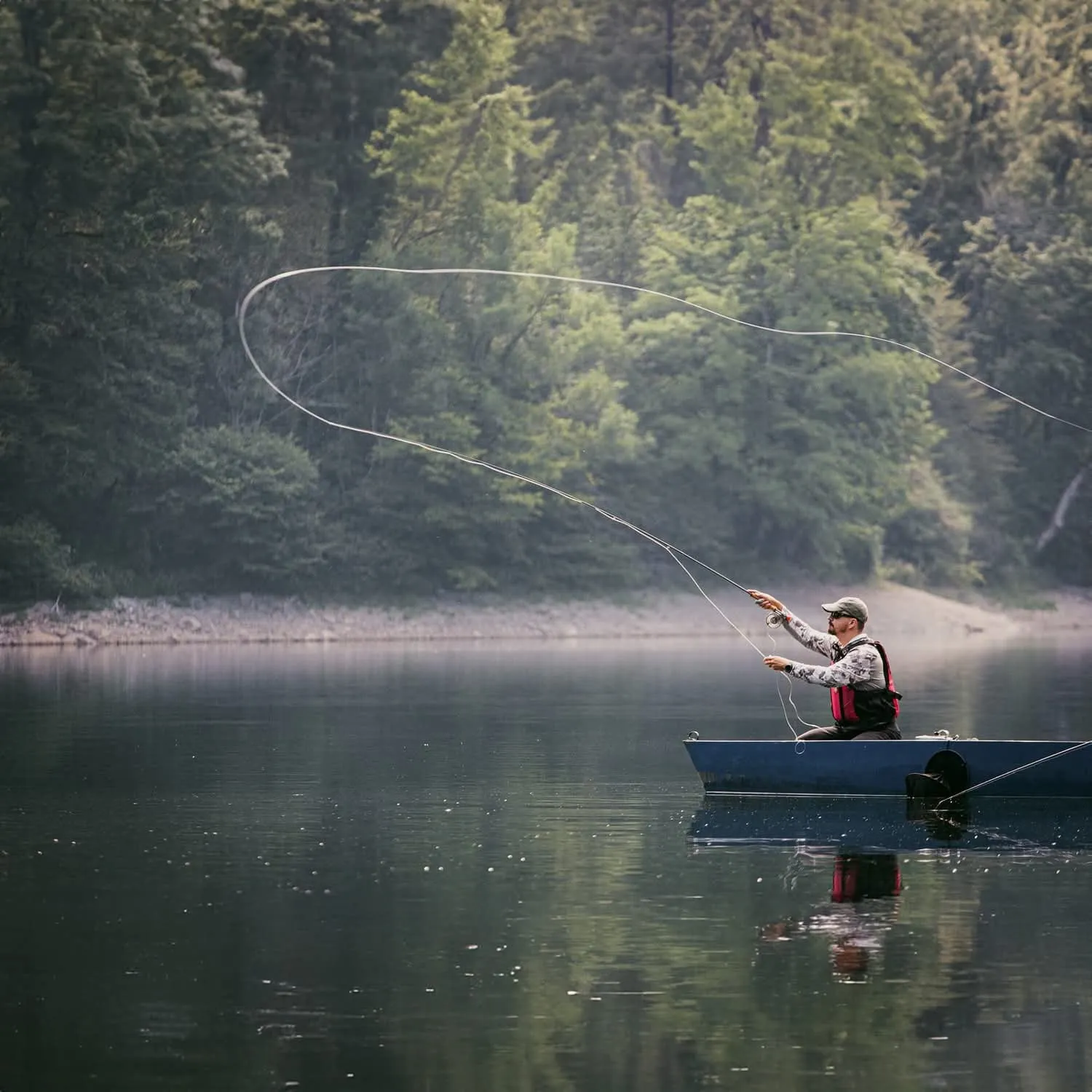 Aleksandar Gasevic casting a long loop of fly line from a boat on a still lake, conifer forest behind.
