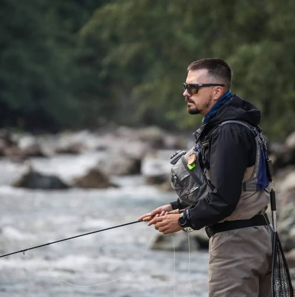Aleksandar Gasevic in profile by a fast river, polarized glasses, fly rod in his hands.